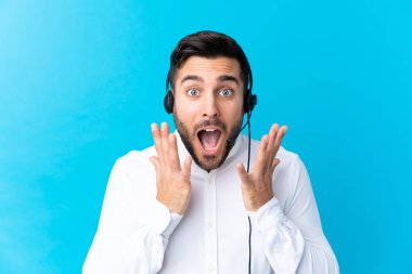 Tele pazarlamacı, mavi arka planda, şaşırtıcı bir yüz ifadesi olan bir kulaklıkla çalışıyor.