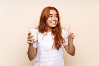 Genç kızıl saçlı kız izole edilmiş arka planda bir bardak süt tutuyor. Çözümü bulmak için parmağını kaldırıyor.