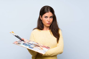 Üzgün ifade ile izole mavi arka plan üzerinde genç sanatçı kadın