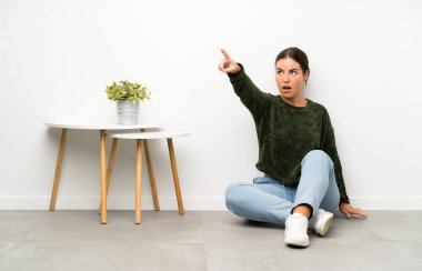 Genç bir kadın yerde oturmuş işaret ediyor.