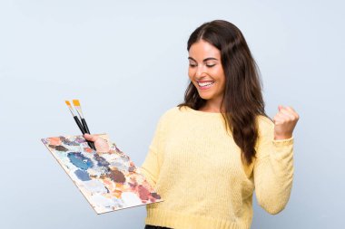 İzole mavi arka plan üzerinde genç sanatçı kadın bir zafer kutluyor