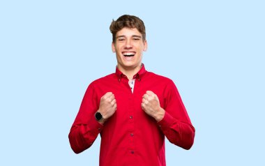 Yakışıklı genç adam izole edilmiş mavi arka planda zaferi kutluyor.