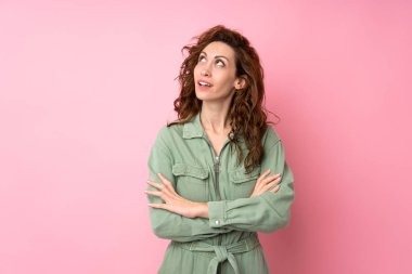 Soyutlanmış pembe arka planda genç ve güzel bir kadın gülümserken yukarı bakıyor