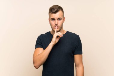 Soyutlanmış arka planda genç, yakışıklı sarışın bir adam sessizlik işareti gösteriyor. Parmağını ağzına sokuyor.