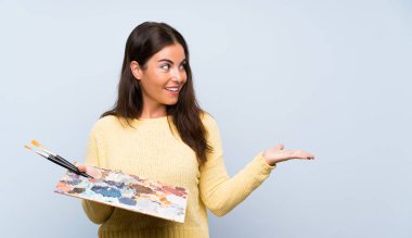 Sürpriz yüz ifadesi ile izole mavi arka plan üzerinde genç sanatçı kadın