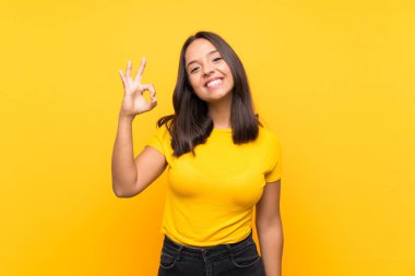 Genç esmer kız izole edilmiş arka planda parmaklarıyla tamam işareti gösteriyor.