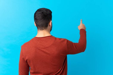 Sakallı, mavi arka planda genç ve yakışıklı bir adam işaret parmağıyla işaret ediyor.