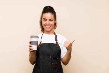 Elinde kahve tutan genç bir kadın bir ürünü sunmak için kenarı işaret ediyor.