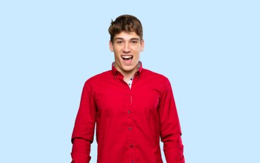 İzole edilmiş mavi arka planda, şaşırmış yüz ifadesi olan yakışıklı bir genç.