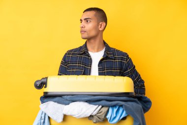 Bir bavul dolusu elbisesi olan gezgin, izole edilmiş sarı arka planda.