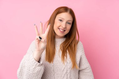 Genç kızıl saçlı kadın pembe arka planda mutlu ve parmaklarıyla üçe kadar sayıyor.