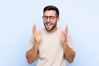 Sakallı, genç ve yakışıklı bir adam mavi arka planda gülüyor.