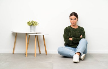 Yerde oturan genç kadın kollarını çapraz tutarak