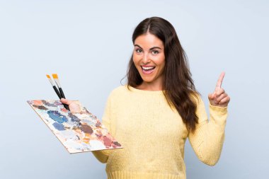 İzole edilmiş mavi arka planda genç bir sanatçı harika bir fikre işaret ediyor.