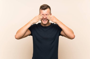Genç yakışıklı sarışın adam izole edilmiş arka planda gözlerini elleriyle kapatıyor.