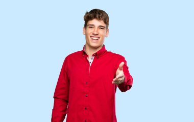 Yakışıklı genç adam, izole edilmiş mavi arka planda iyi bir anlaşmadan sonra el sıkışıyor.