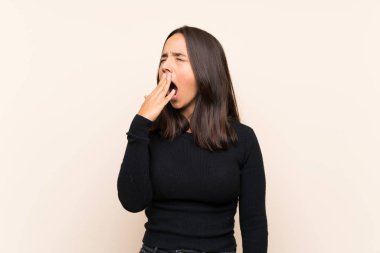 İzole edilmiş arka planda beyaz kazaklı esmer kadın esniyor ve ağzını eliyle kocaman açık tutuyor.