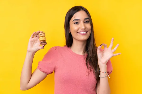 Jovem Morena Sobre Fundo Amarelo Isolado Segurando Macarons Franceses Coloridos — Fotografia de Stock