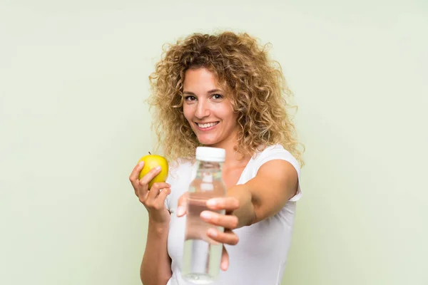 Jeune femme blonde aux cheveux bouclés avec une pomme et une bouteille d'eau — Photo