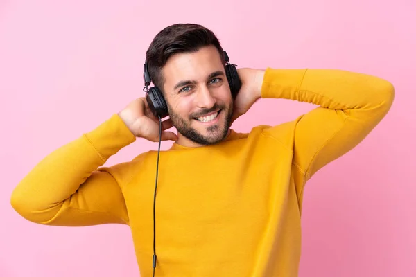 Joven hombre guapo con barba escuchando música sobre rosa aislado — Foto de Stock