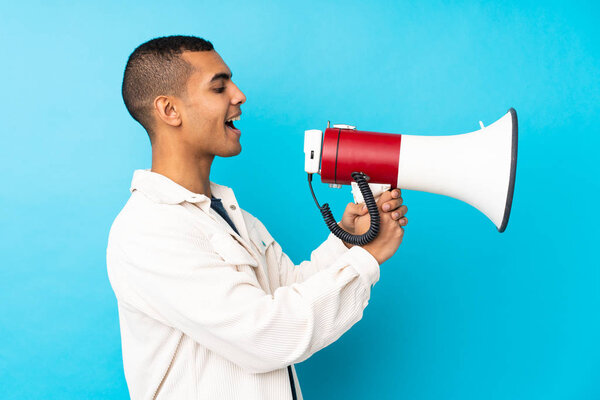 Молодой афроамериканец на изолированном синем фоне кричит через мегафон
