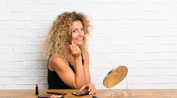 Mujer joven con mucho cepillo de maquillaje en una mesa — Foto de Stock