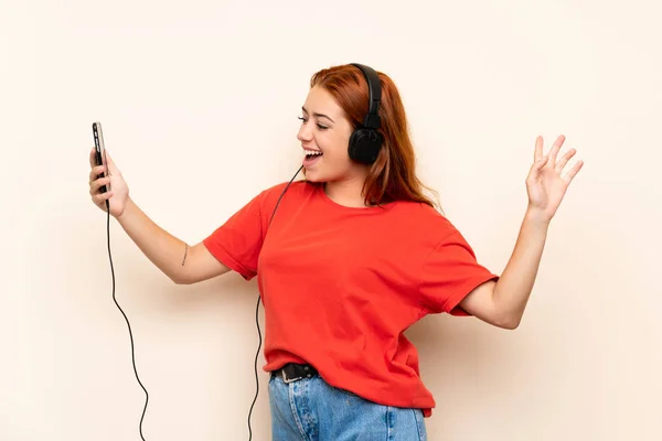 Adolescente rousse fille écoute de la musique avec un mobile sur fond isolé — Photo