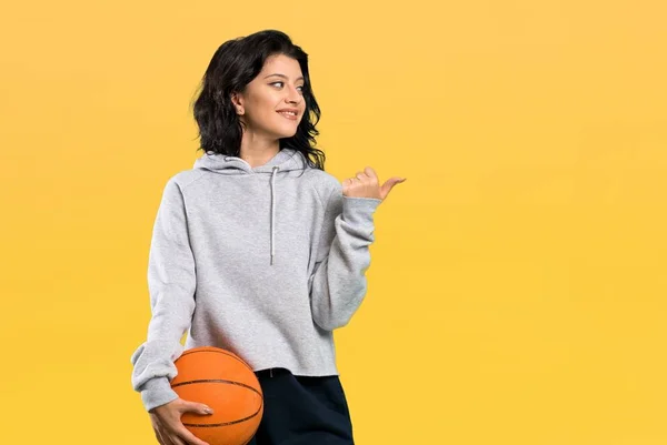 Młoda Kobieta Gra Koszykówkę Wskazując Bok Aby Przedstawić Produkt Odosobnionym — Zdjęcie stockowe