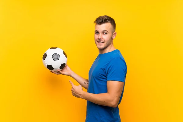 Młody Przystojny Blondynka Człowiek Trzyma Piłka Nożna Odizolowany Żółty Tło — Zdjęcie stockowe