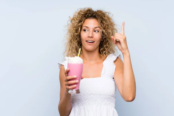 年轻的金发女人 卷曲的头发 拿着草莓奶昔 想在举起一只手指头的同时实现这个解决方案 — 图库照片