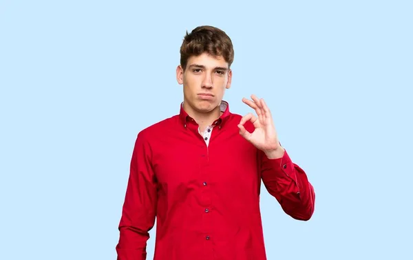 Przystojny Młody Człowiek Pokazuje Znak Palcami Nad Odizolowanym Niebieskim Tle — Zdjęcie stockowe
