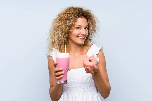 Jeune femme blonde aux cheveux bouclés tenant un milkshake aux fraises et un beignet — Photo