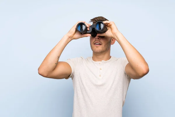 Joven Guapo Hombre Rubio Sobre Fondo Azul Aislado Con Binoculares — Foto de Stock