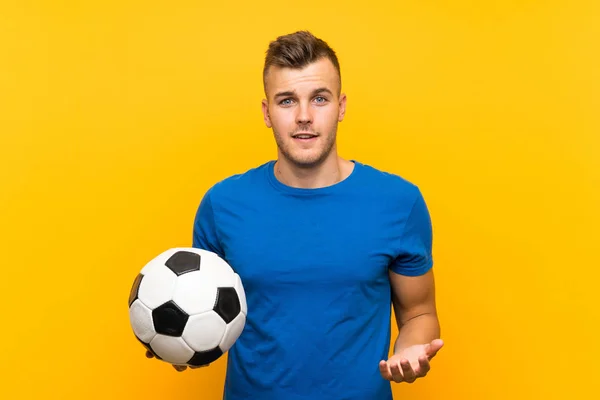 Młody Przystojny Blondynka Człowiek Trzymając Piłka Nożna Odizolowany Żółty Tło — Zdjęcie stockowe