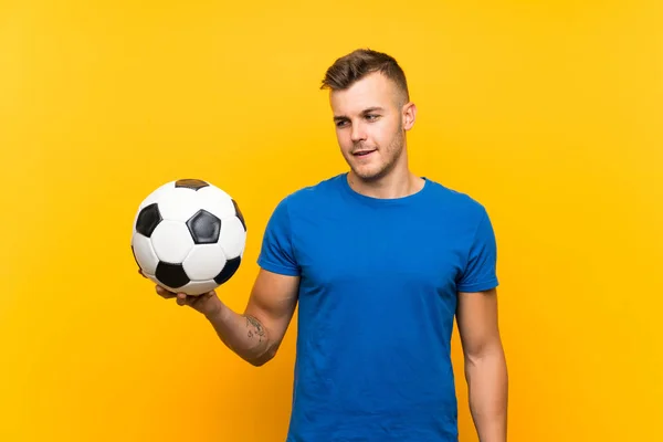 Młody Przystojny Blondynka Mężczyzna Trzymanie Piłki Nożnej Białym Tle Żółty — Zdjęcie stockowe