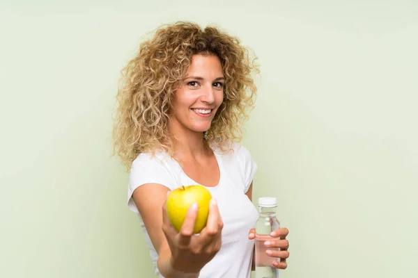 Ung blond kvinna med lockigt hår med ett äpple och med en flaska vatten — Stockfoto