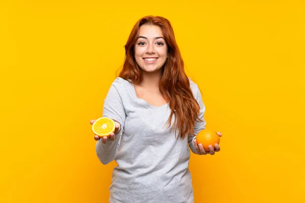 Genç kızıl saçlı kız izole sarı arka plan üzerinde bir portakal tutan — Stok fotoğraf