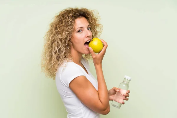 Fiatal szőke nő göndör haja almával és egy üveg vízzel — Stock Fotó