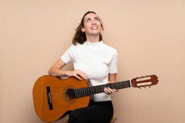 Arka planda gitar çalan genç bir kadın gülümserken yukarı bakıyor.