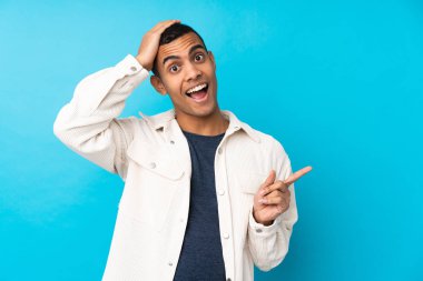 Genç Afro-Amerikalı adam mavi arka planda şaşırdı ve parmağını yana çevirdi.