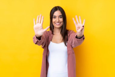 Genç esmer kadın izole edilmiş sarı arka planda dokuz parmaklı sayıyor.