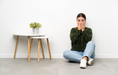 Genç bir kadın yerde oturuyor ve yüzünde sürpriz bir ifade var.