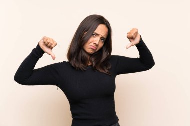 İzole edilmiş arka planda beyaz kazaklı esmer bir kadın baş parmağını aşağı gösteriyor.