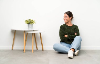 Genç bir kadın yerde oturuyor, yan tarafa bakıyor.