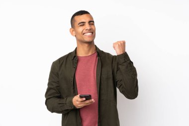 Genç Afrikalı Amerikalı, izole edilmiş beyaz arka planda, telefon zafer pozisyonunda.