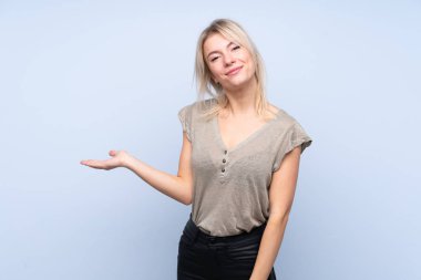 İzole edilmiş mavi arka plan üzerinde genç sarışın bir kadın. Kopyalama alanı hayali avuçlarında tutuyor.