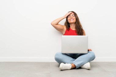 Yerde oturan dizüstü bilgisayarı yla gülen genç kadın