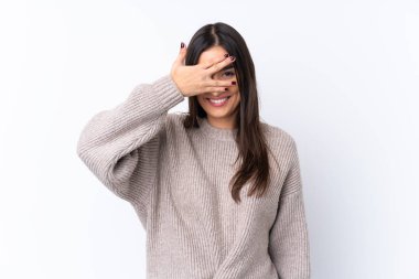 İzole edilmiş beyaz arka planda genç esmer kadın. Gözleri elleriyle kaplıyor ve gülümsüyor.