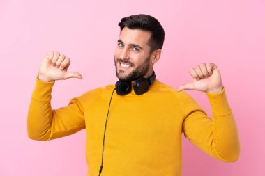 Soyutlanmış pembe arka planda kulaklıkları olan genç yakışıklı bir adam gururlu ve kendini beğenmiş.