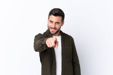 İzole edilmiş beyaz arka planda sakallı yakışıklı genç adam kendine güvenen bir ifadeyle seni işaret ediyor.